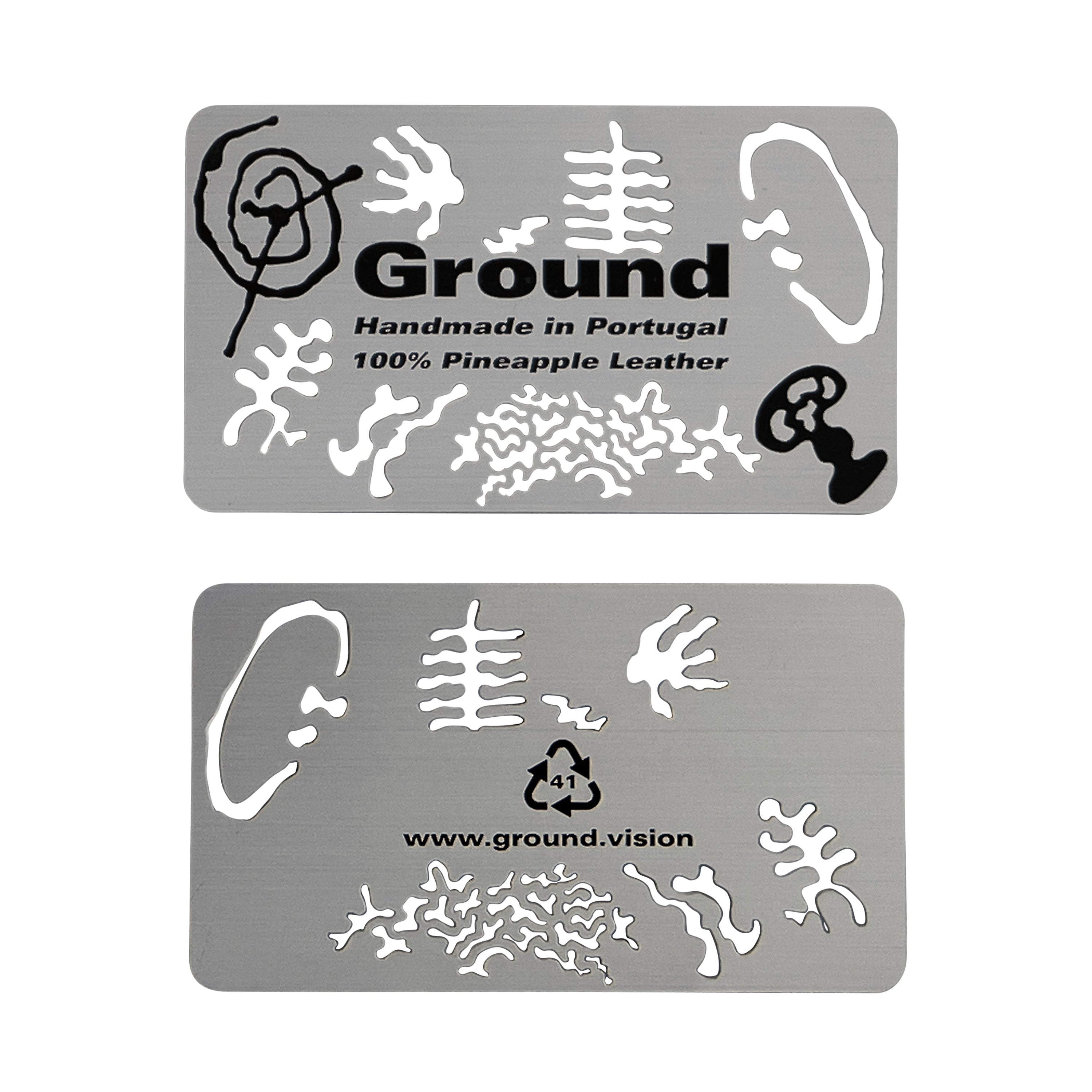 The metal cards included in every Ground wallet order that have petroglyph-like shape cutouts as well as printed shapes, the aluminum 41 recycling symbol, and the text: Ground Handmade in Portugal 100% Pineapple Leather www.ground.vision